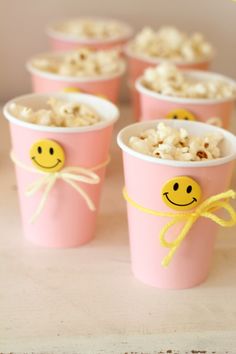 pink cups with smiley faces on them are sitting on a table next to some popcorn