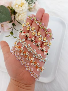 the hand is holding several bracelets with flowers on them and beads in different colors