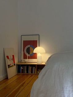 a white bed sitting next to a lamp on top of a wooden floor