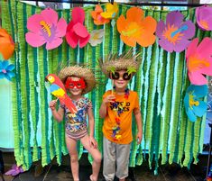 two young children standing next to each other in front of a wall with paper flowers