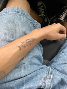 a person with a fish tattoo on their arm sitting in a car holding a cell phone