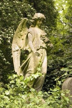 an angel statue standing in the middle of a lush green forest next to two headstones