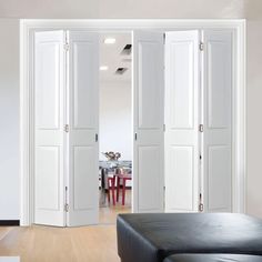 an open room with white doors and black leather couch in the foreground is a dining table