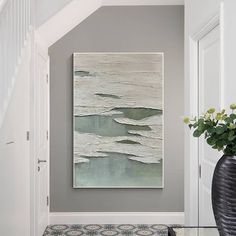 an abstract painting hangs on the wall next to a vase with white flowers in it