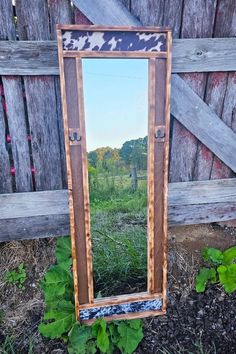 a mirror sitting on the ground in front of a wooden fence with plants growing next to it