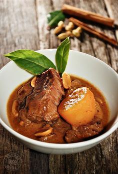 a white bowl filled with meat and gravy on top of a wooden table