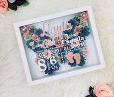 a baby announcement is displayed in a shadow box on a white furnishing next to flowers