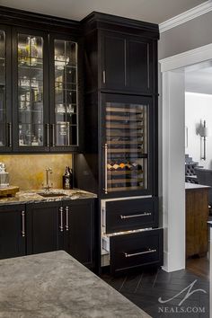 a kitchen with black cabinets and marble counter tops, an island in the middle has wine glasses on it