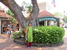 a woman standing next to a tree in front of a building with shops on it