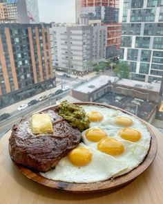 two eggs and some meat are on a plate in front of a cityscape