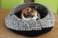 a cat laying in a crocheted bed on top of a wooden table