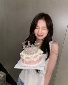 a woman holding a cake with pearls on it and wearing a tiara in front of her face