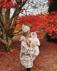 a woman holding a baby in her arms while walking through an autumn tree filled with leaves