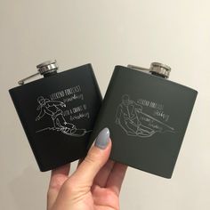 two black flasks with white writing are held up in front of each other