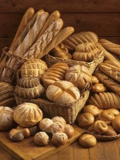 a painting of breads and buns on a wooden table next to a basket