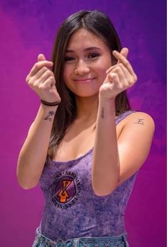 a girl with her hands up in the air and smiling at the camera while standing against a purple background