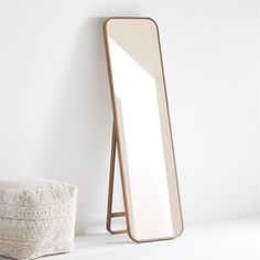 a mirror sitting on top of a white floor next to a basket and towel dispenser