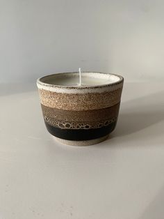 a small candle sitting on top of a white table next to a black and brown striped cup