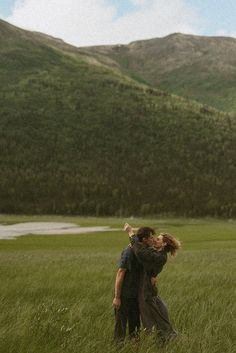 two people standing in a field with mountains in the background