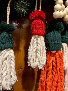 three tasseled hats hanging from strings on a wooden wall with pine cones in the background