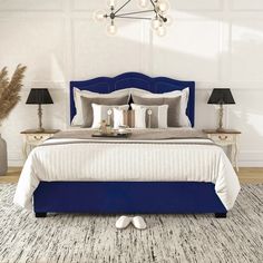 a bed with blue headboard and foot stools in a white room next to two lamps