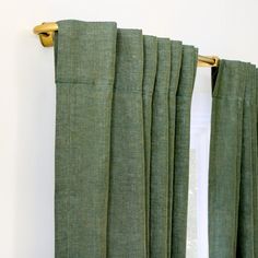 green curtains hanging on the side of a white wall with gold hardware and curtain rods