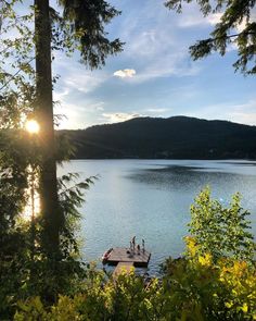 the sun shines brightly through the trees over a lake with a dock in the foreground