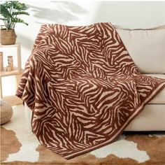 a brown and white zebra print blanket sitting on top of a couch next to a potted plant