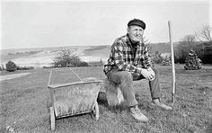 a man sitting on top of a wooden wheelbarrow next to a small cart