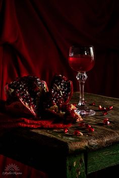 a glass of wine sitting on top of a table next to pomegranate