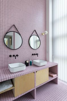 two sinks and mirrors in a bathroom with pink tiles on the walls, along with other accessories