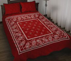 a red bedspread with a white border and paisley print on the edges, in front of a window