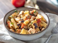 a bowl filled with pasta and meat on top of a napkin next to an apple