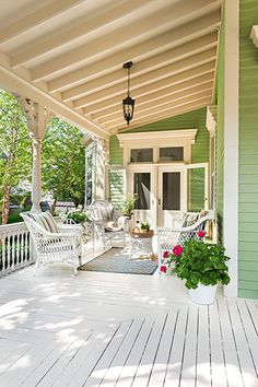 a porch with chairs and potted plants on the front steps, next to a green house