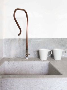 two coffee mugs sitting on top of a concrete sink next to a faucet