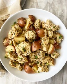 a white bowl filled with potatoes and meat on top of a wooden table next to a napkin