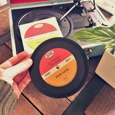 a person holding up a record on top of a wooden table next to a potted plant