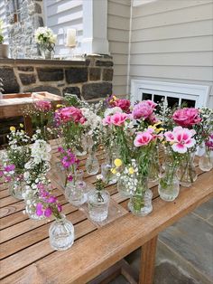 a wooden table topped with lots of glass vases filled with flowers on top of it