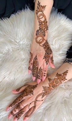 two hands with henna tattoos on them sitting on top of a fluffy white rug