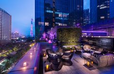 an outdoor seating area in the middle of a city at night with lit up buildings and skyscrapers