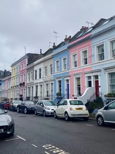 several cars parked on the street in front of multi - colored houses with white windows