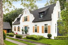 a white house with brown shutters on the front and side windows, along with green grass