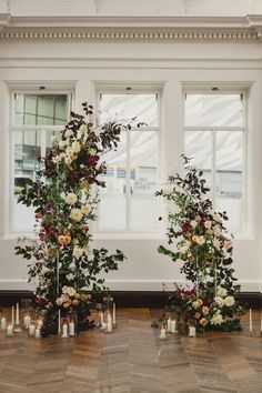 an arrangement of flowers and candles in front of two windows on the floor next to each other