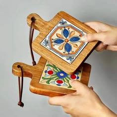 two hands holding an ornate wooden box with colorful designs on the lid and sides, while another hand holds a string attached to it