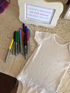 a baby's bodysuit, crayons and markers are on the table