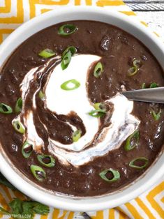 a white bowl filled with black bean soup and topped with sour cream, green onions and jalapenos