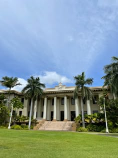 a large building with columns and palm trees in front of it on a sunny day