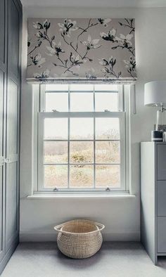 a basket sitting on the floor in front of a window with roman shades over it