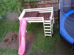 there is a pink slide next to the pool and a blue trampoline in the back yard