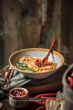 a bowl filled with noodles and vegetables next to chopsticks on a wooden table